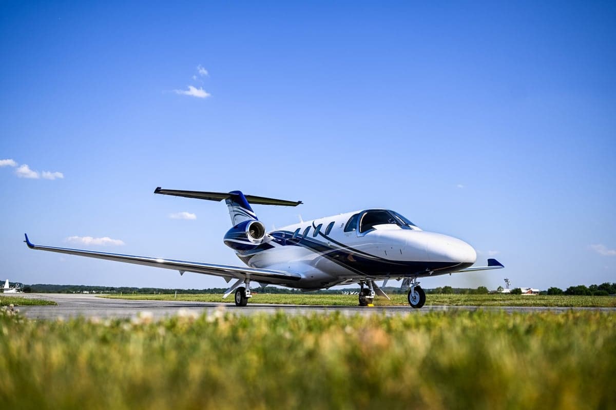 A low-angle view of a white and blue Cessna Citation M2 jet on an airport tarmac.