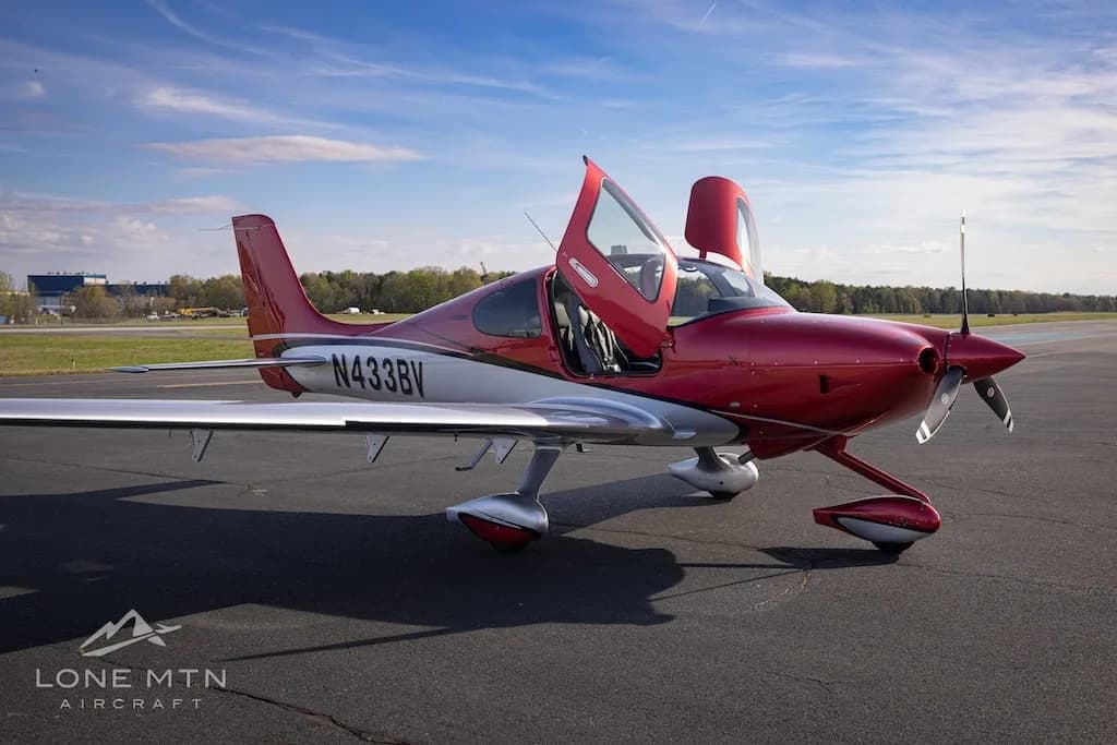 A red and silver Cirrus SR22 aircraft with registration N433BV parked on an airfield with its doors open.