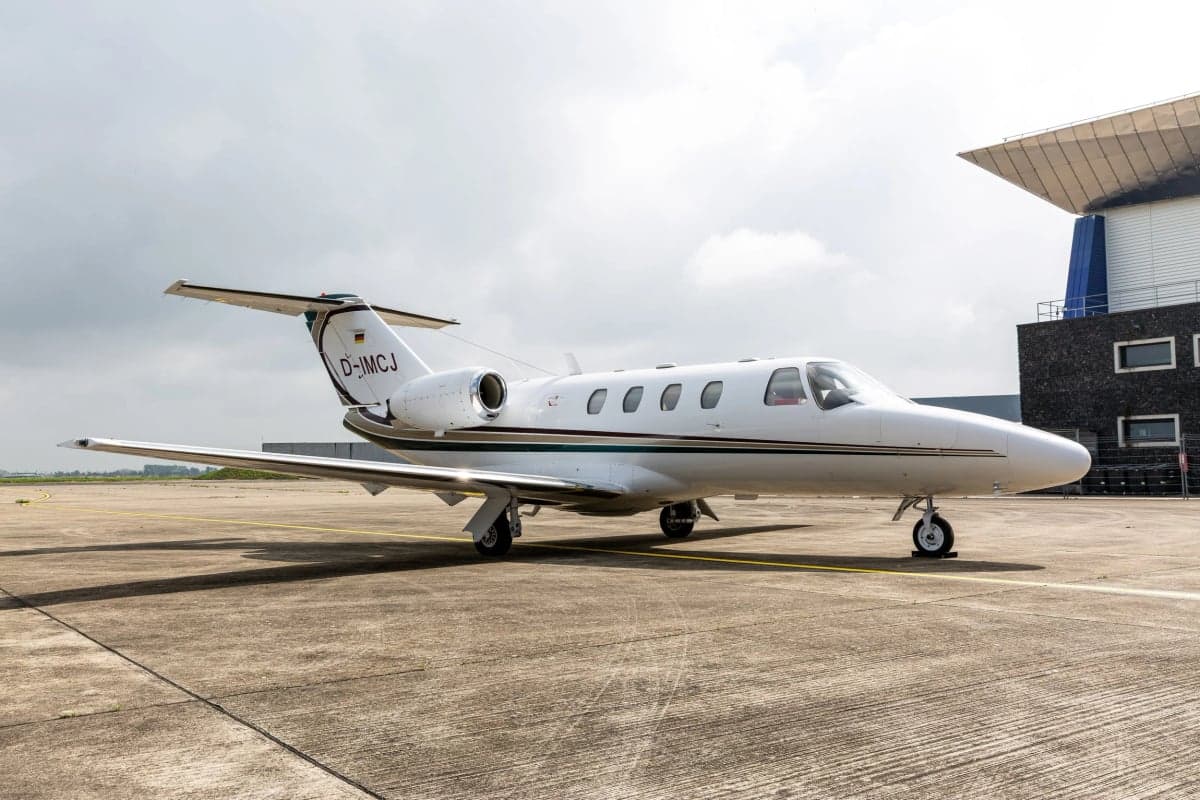 A white and green Cessna CitationJet (CJ1) with registration D-IMCJ parked on a tarmac next to a modern building.
