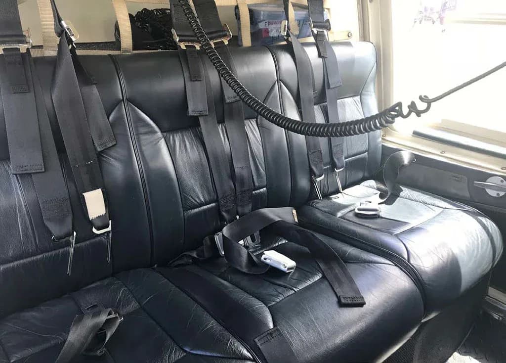 Interior view of the helicopter's rear cabin with black leather seats and multiple seatbelts.