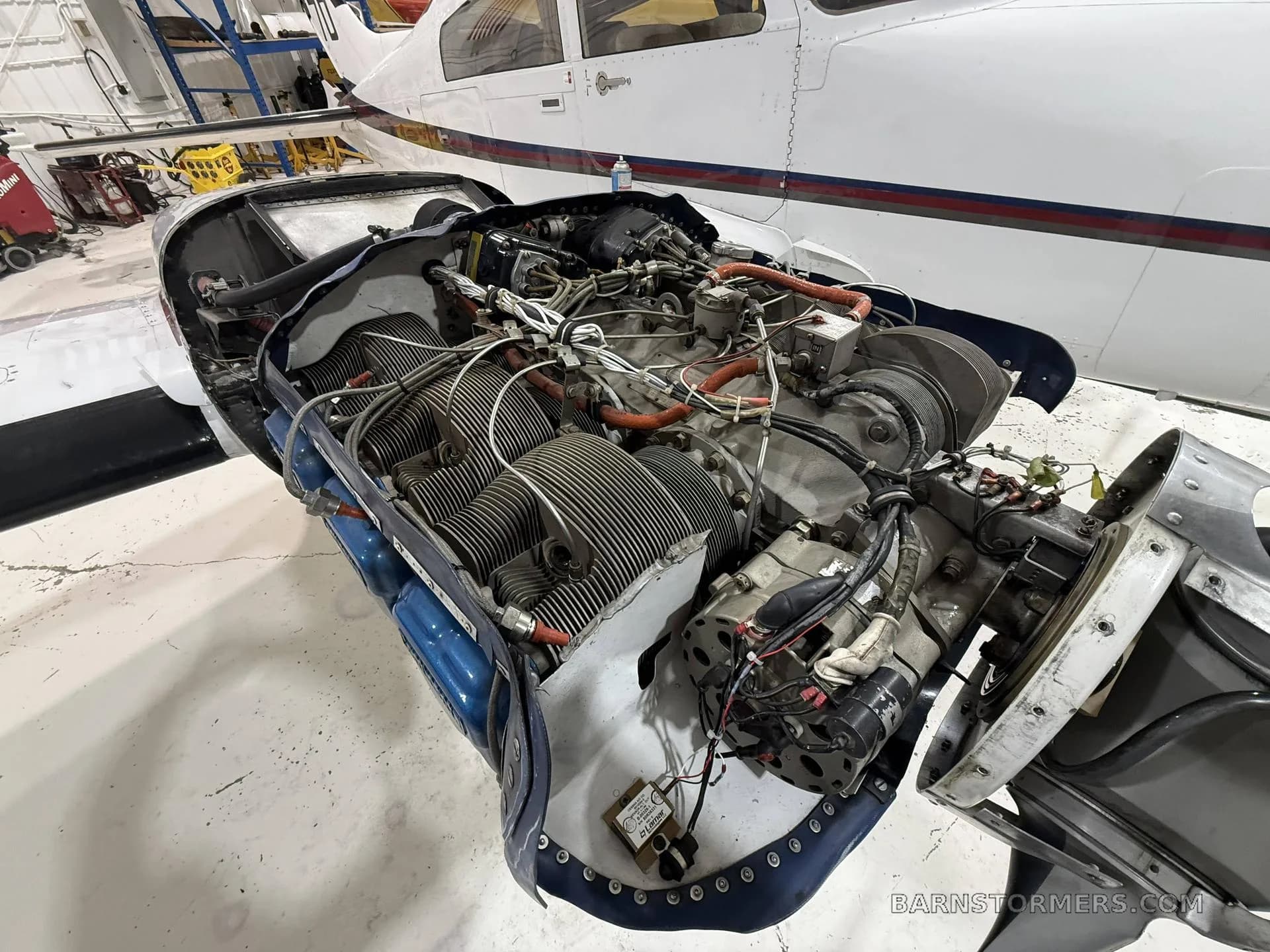 An angled view of a Continental aircraft engine with its cowling removed, showing cylinders and the propeller hub, in a hangar.