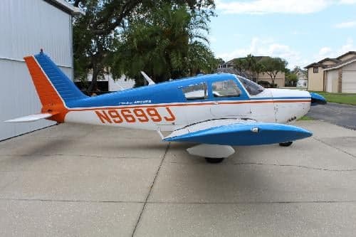 Side view of a Piper Archer aircraft with blue and white paint scheme and tail number N9699J.