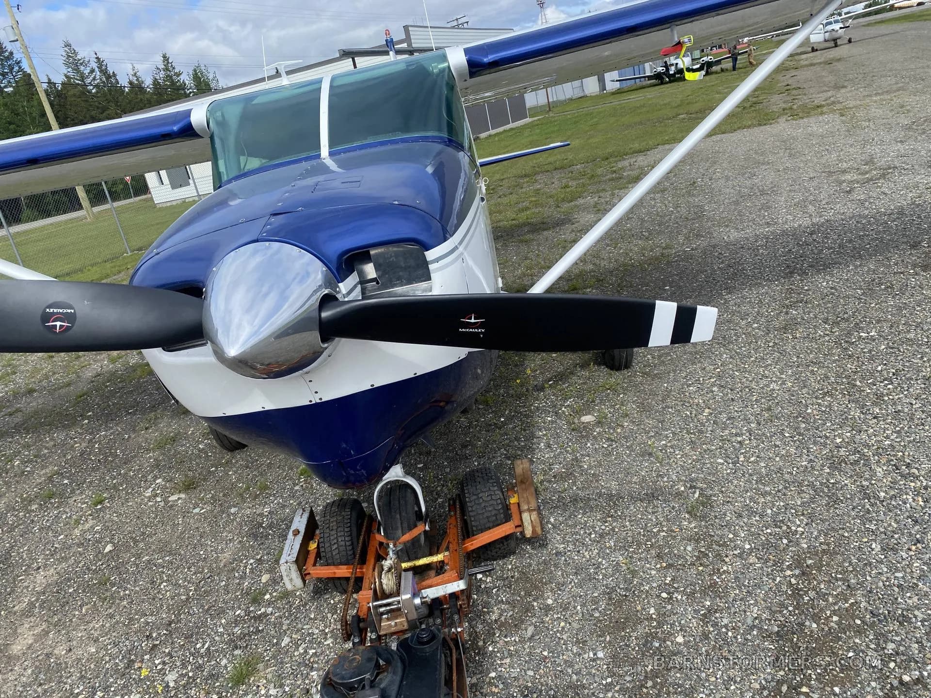 A front view of a blue and white single-engine aircraft with a tow bar on a gravel lot.