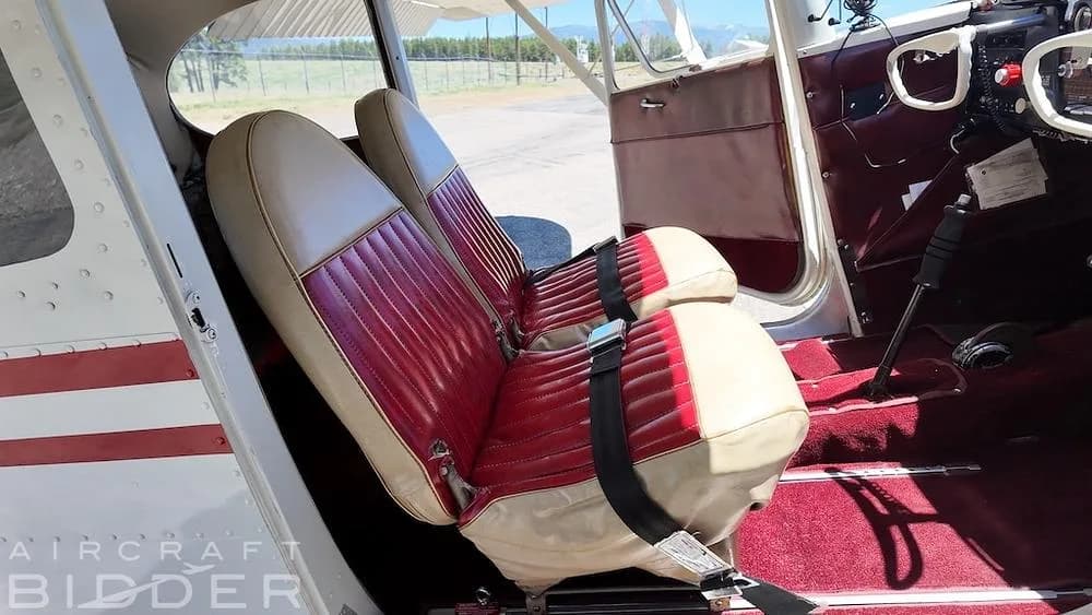 The interior cabin of a 1950 Cessna 170A, showing two red and tan upholstered seats with seatbelts.