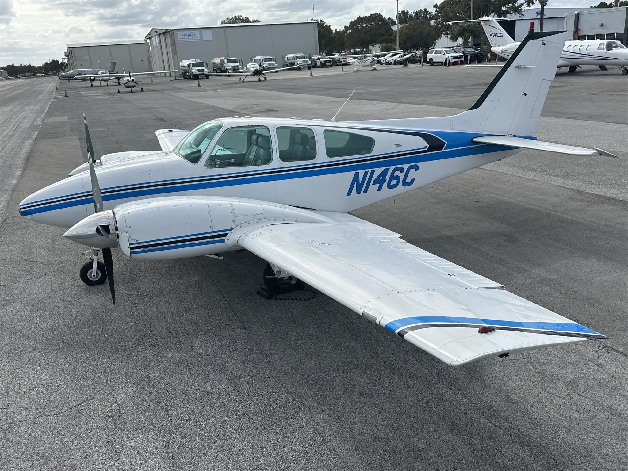 A white and blue twin-engine aircraft, N146C, parked on an airport tarmac with hangars in the background.