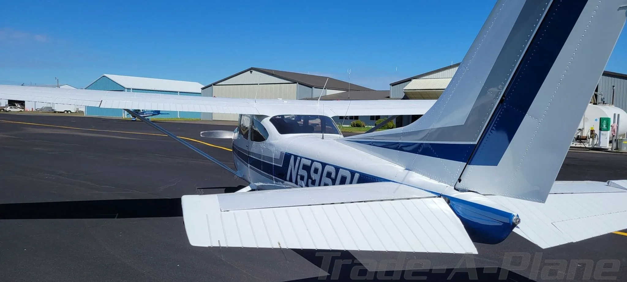 Rear view of a white and blue Cessna 182 Skylane aircraft parked on an airfield tarmac.