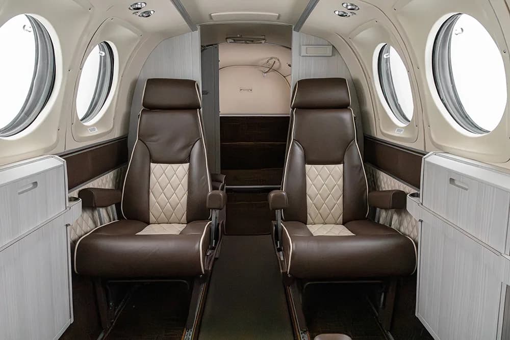 Two brown and beige quilted aircraft seats facing forward in the cabin, with a lavatory or storage area visible at the rear.