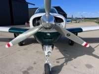 A Beechcraft Bonanza with a white and green paint scheme is parked on the tarmac.