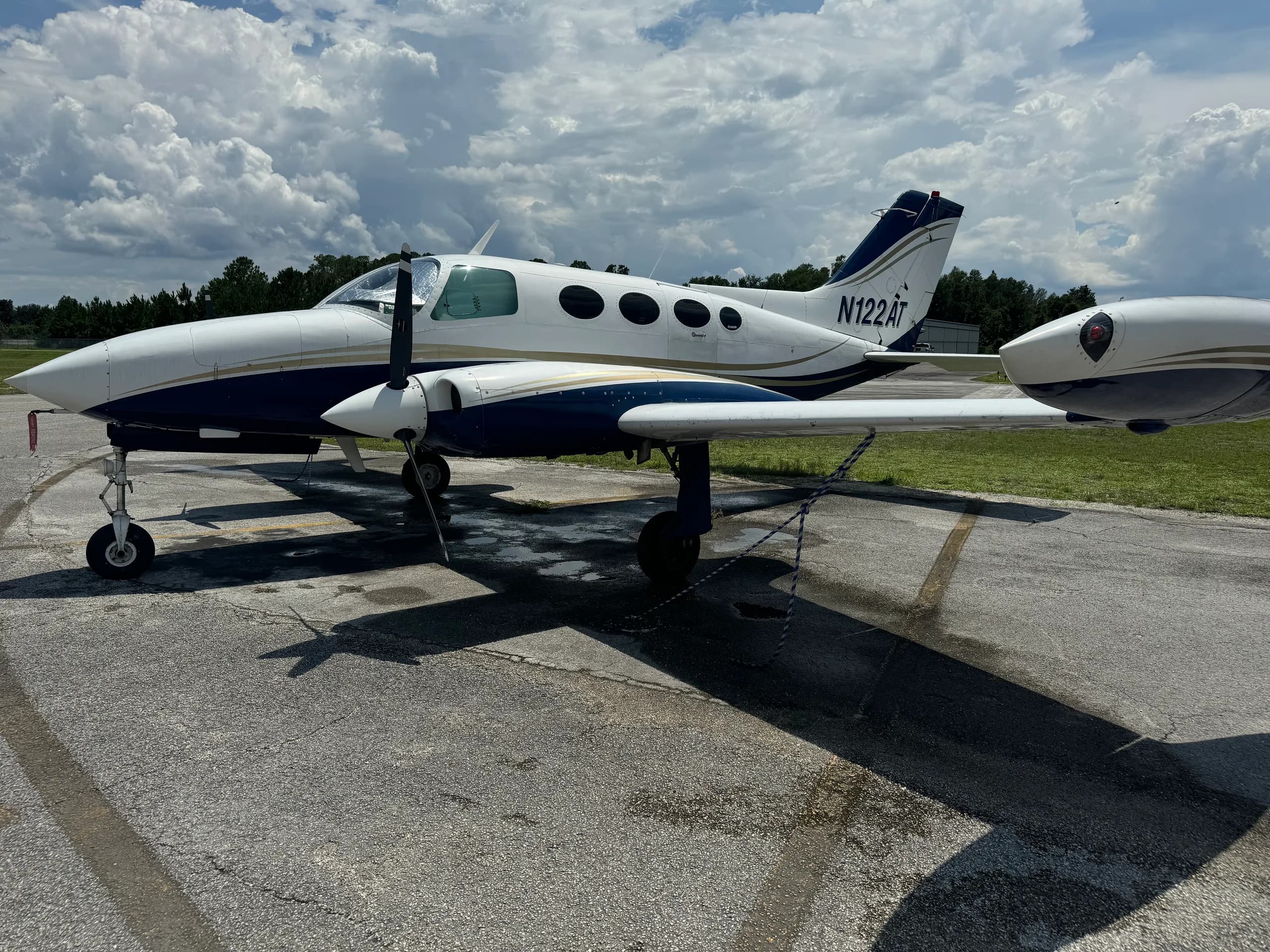 Rear-side view of a white and blue Cessna 401 (or similar twin-engine prop) aircraft, registration N122AT, parked on an airport ramp.
