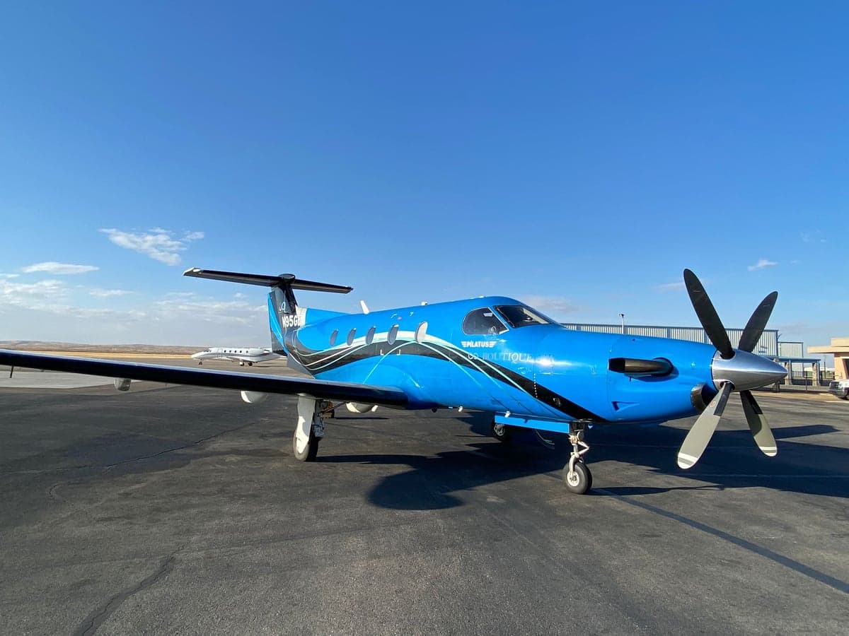 A blue Pilatus PC-12 aircraft with black stripes parked on the ramp.