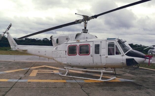 A white Bell 212 helicopter on a helipad with another helicopter in the background.
