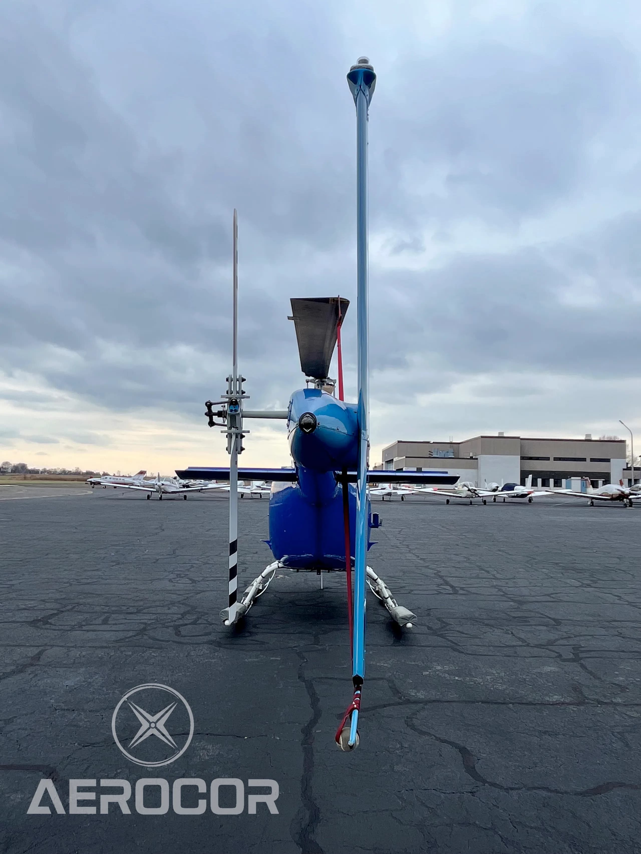 A rear view of the blue and white Bell JetRanger III helicopter, tail number N411DD, showing the tail rotor and vertical stabilizer on an airfield.