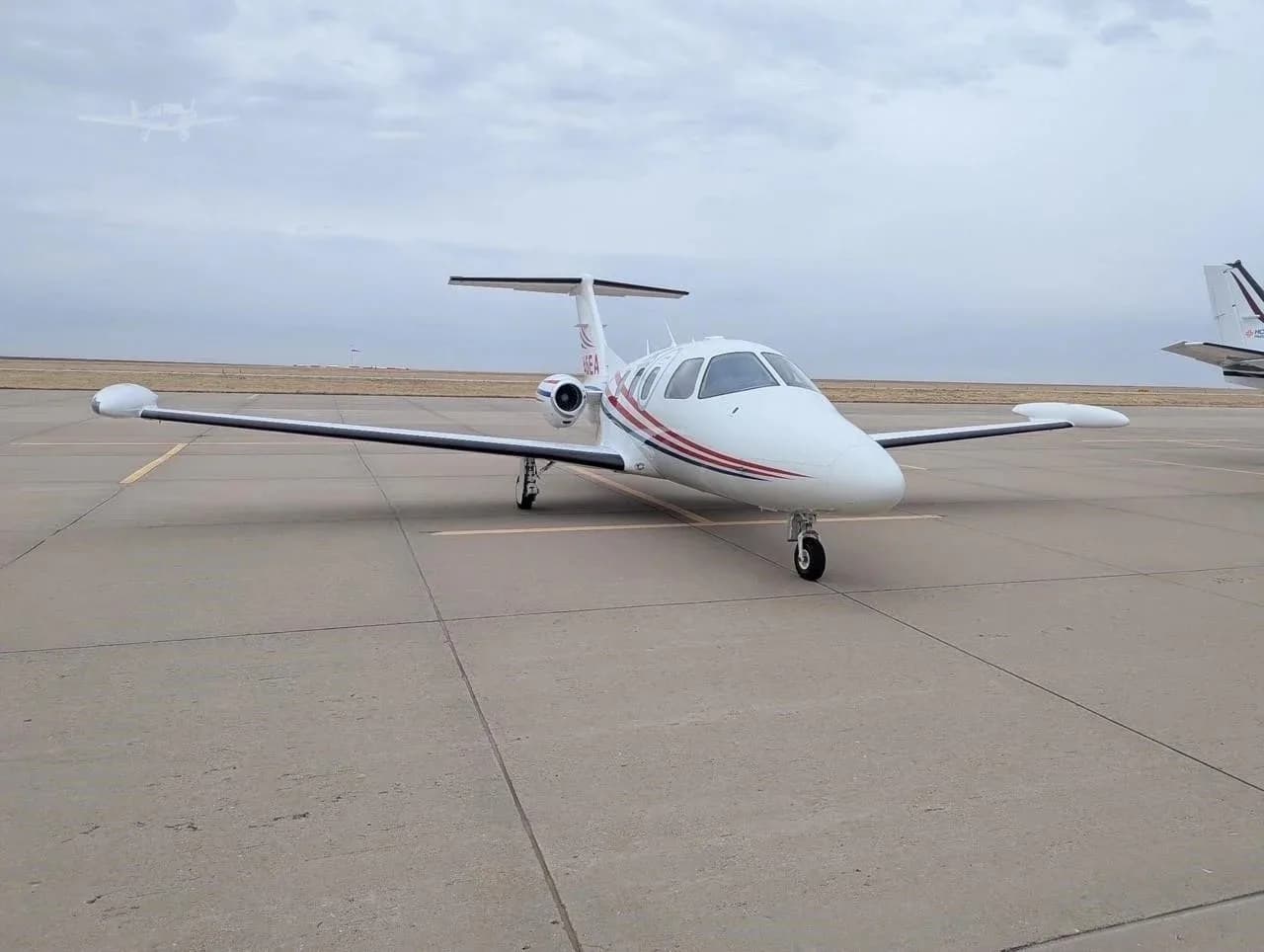 A white Eclipse jet with red and blue stripes parked on an airfield, viewed from the front-right.