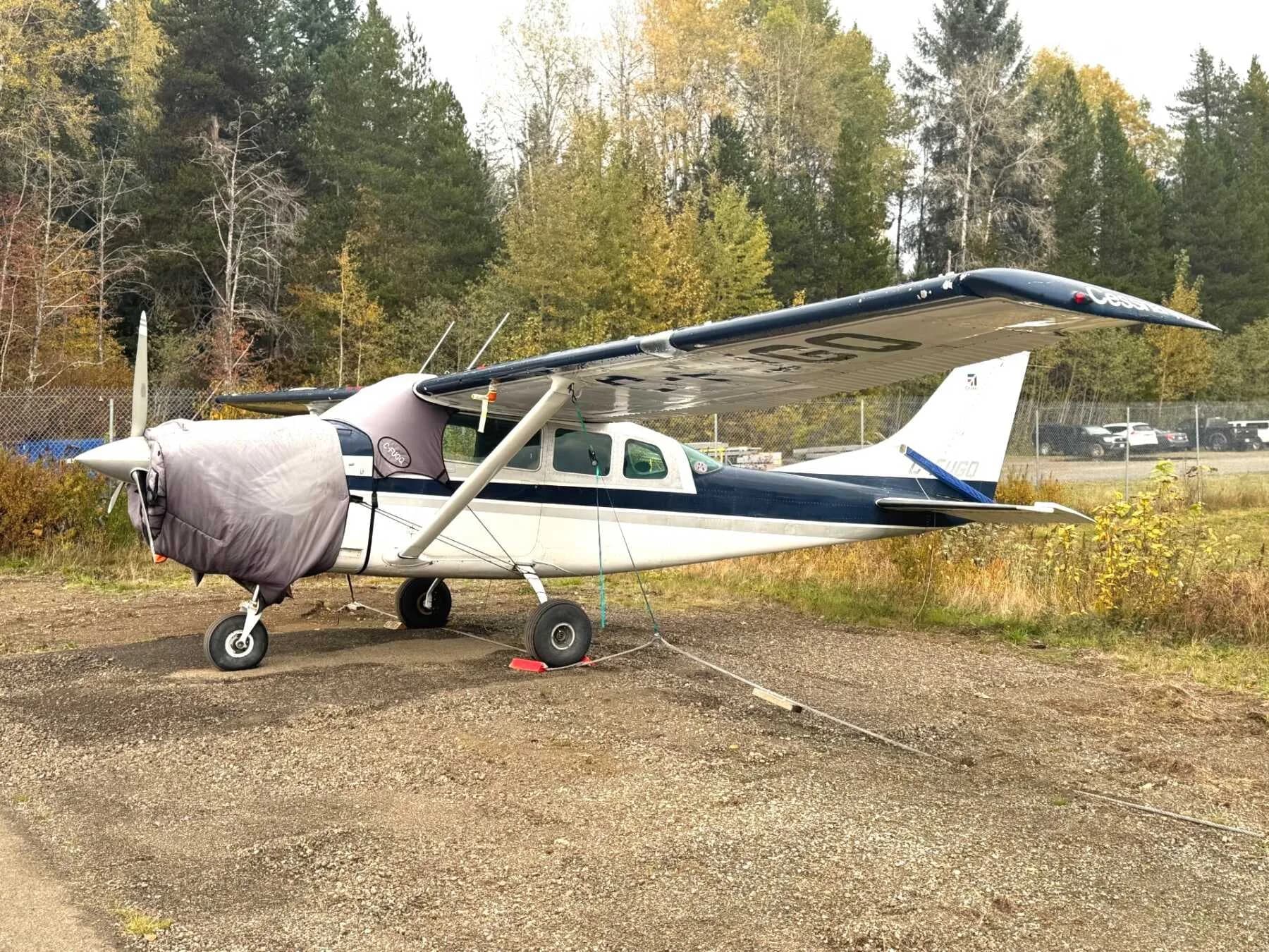 A Cessna 206 Stationair parked on a gravel area with a cover on the engine.