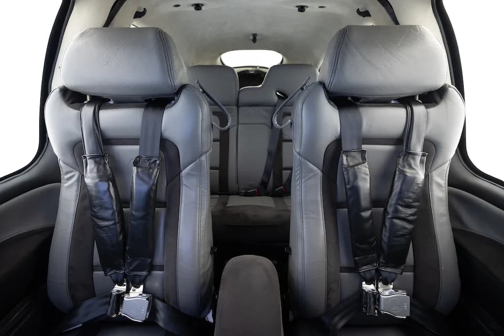 The gray leather front seats of an aircraft cabin with seatbelts fastened.