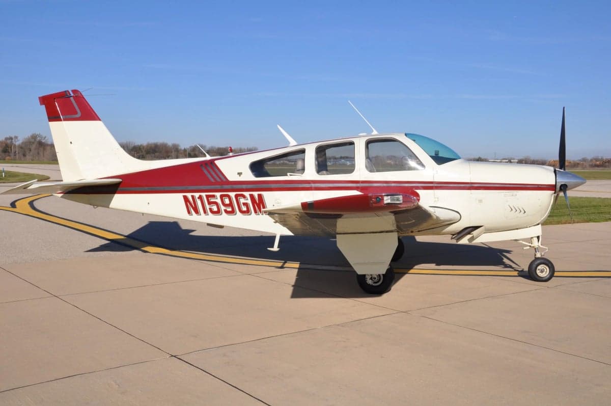 Side view of a Beechcraft Bonanza with a red and white paint scheme on the tarmac.