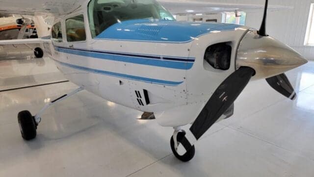 A Cessna Centurion aircraft with a blue and white paint scheme is parked inside a hangar.