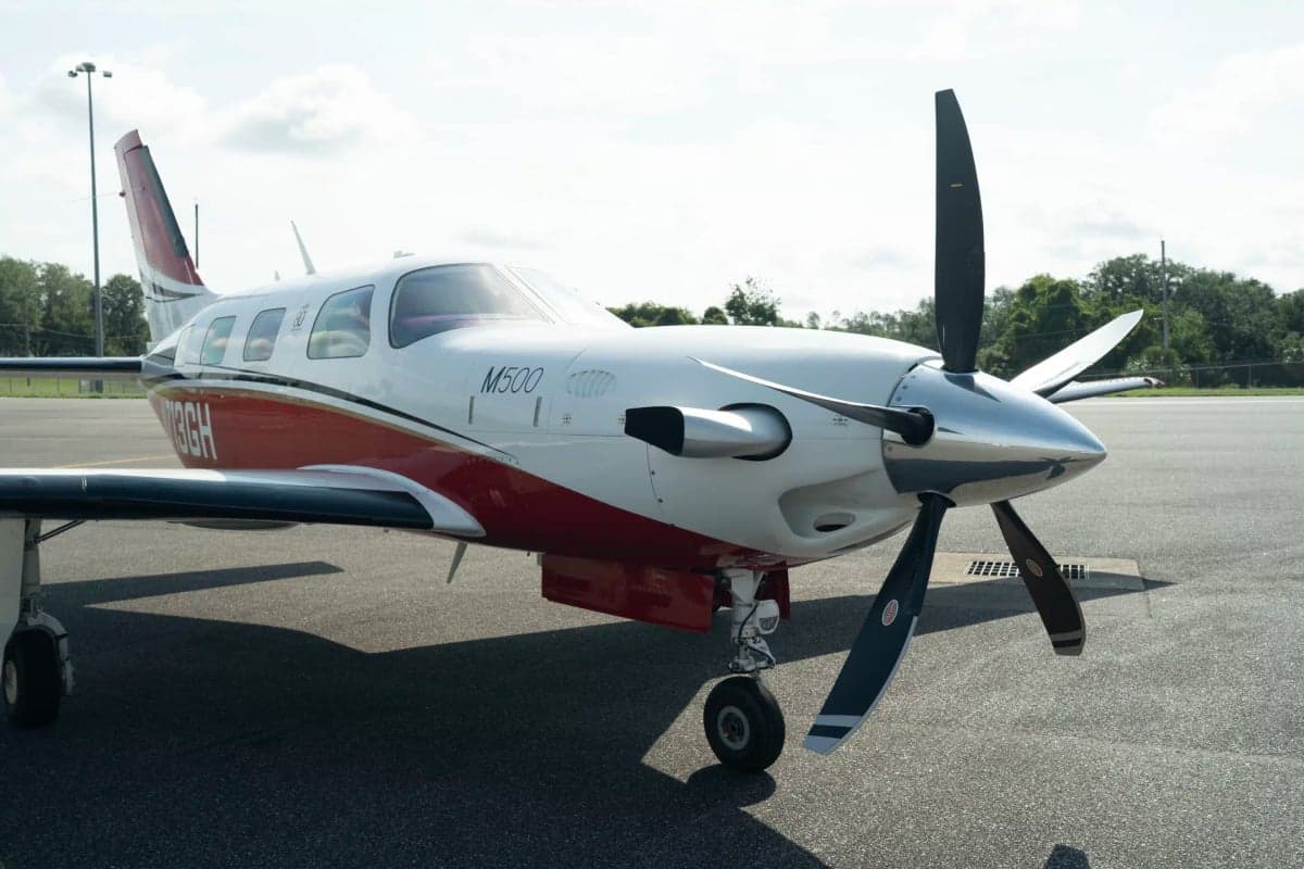A close-up view of the front of a white and red Piper M500 aircraft with its propeller and landing gear.