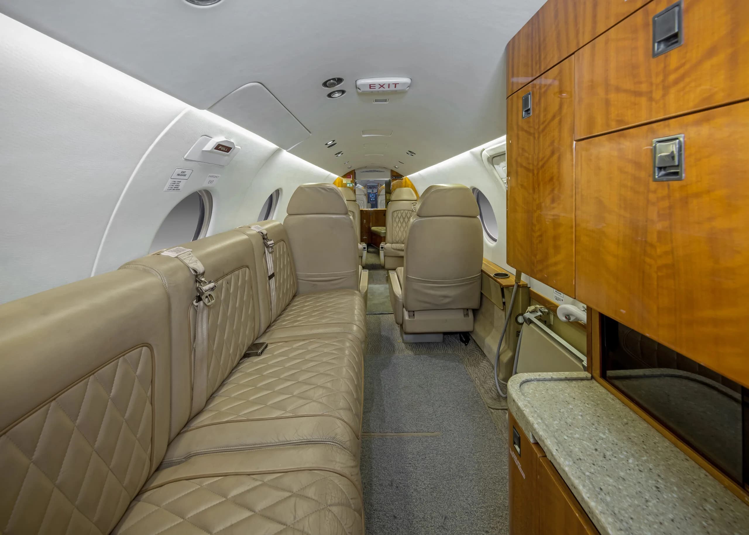 View of the aircraft interior with tan leather seats and wooden cabinetry.
