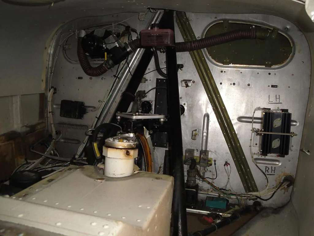An internal view of an aircraft's utility compartment, showing exposed wiring, structural elements, and various components.