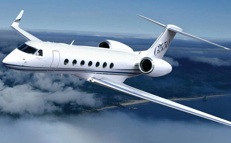 A Gulfstream G550 in flight over clouds and water.