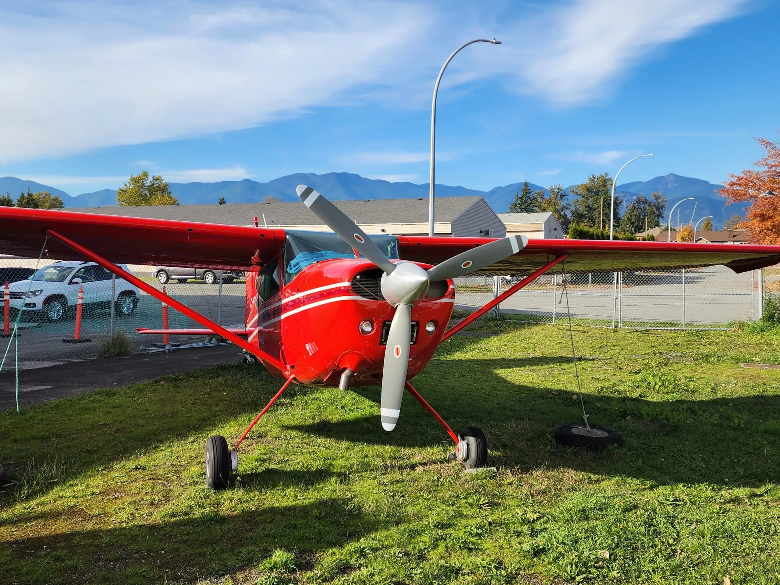 Front view of a red and white Cessna aircraft with a three-blade propeller parked on grass.