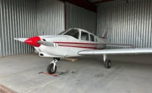 A small aircraft with a red nose parked inside a hangar.
