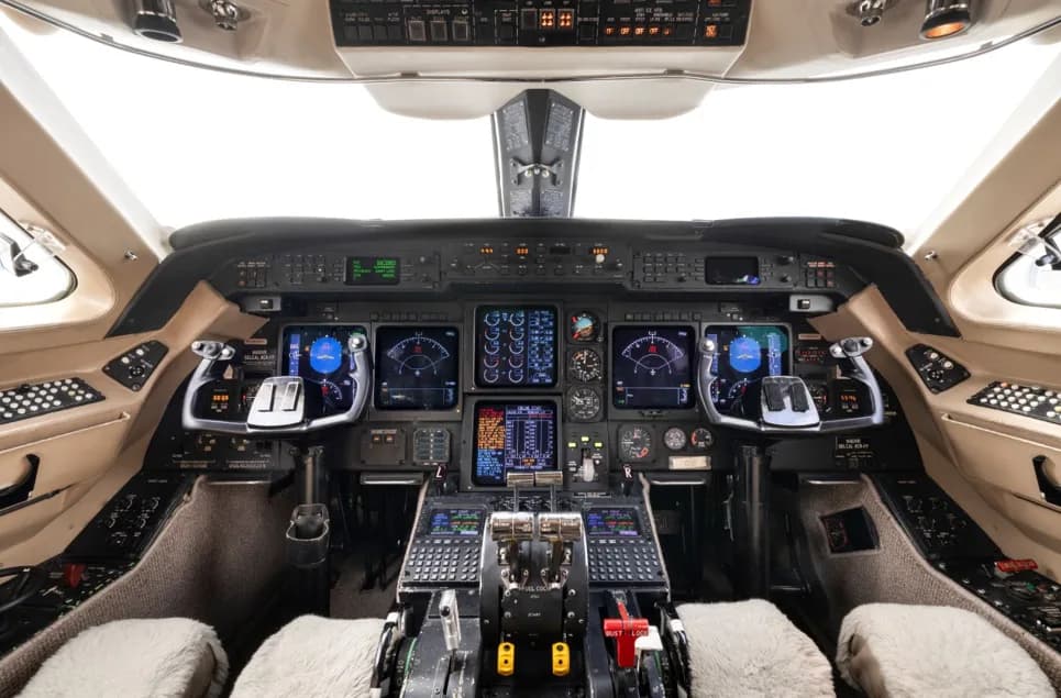 The modern cockpit of a business jet featuring multiple digital displays and a complex control panel.
