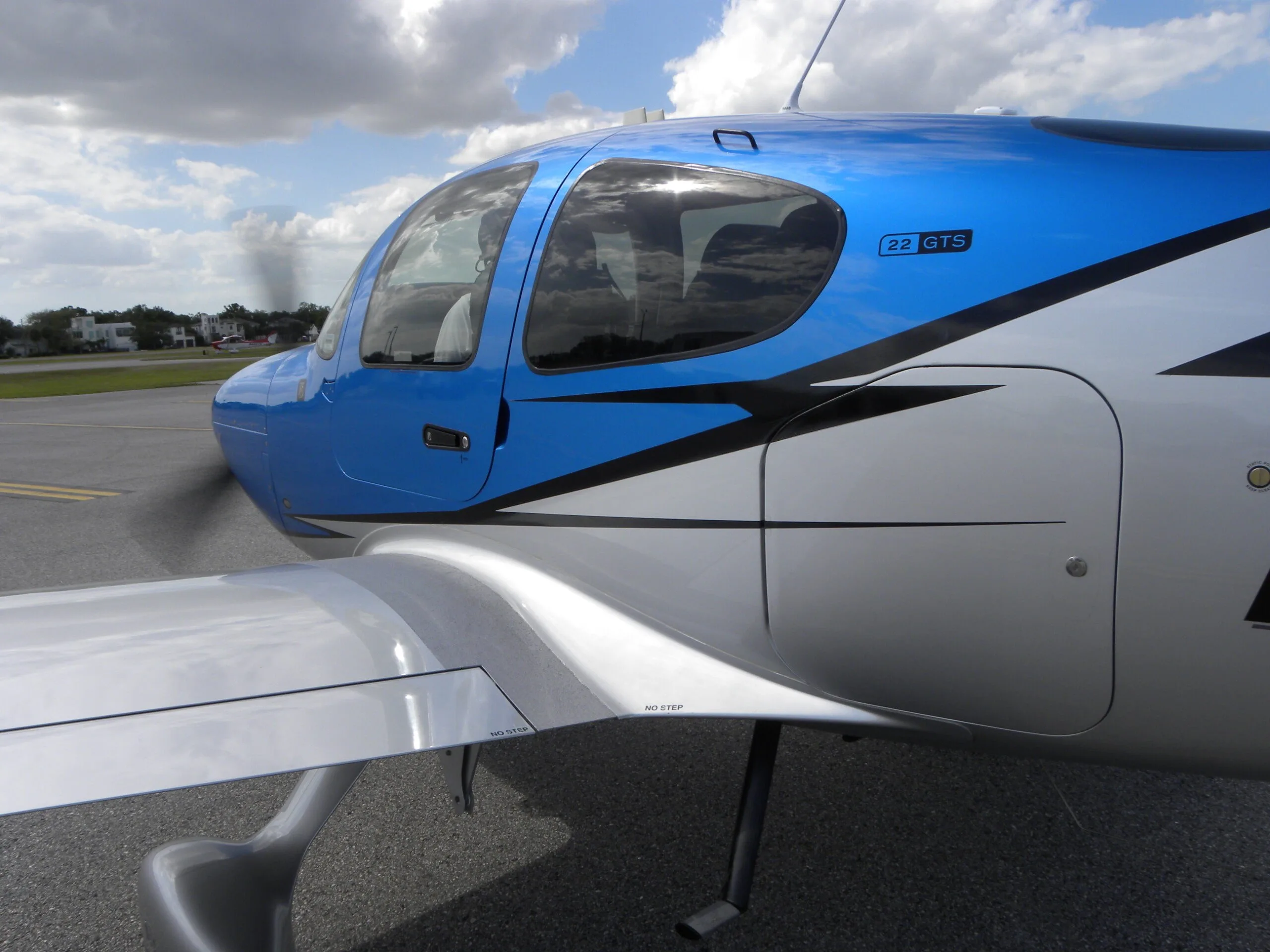 A close-up view of the cockpit and front fuselage of a blue and silver Cirrus SR22 aircraft.