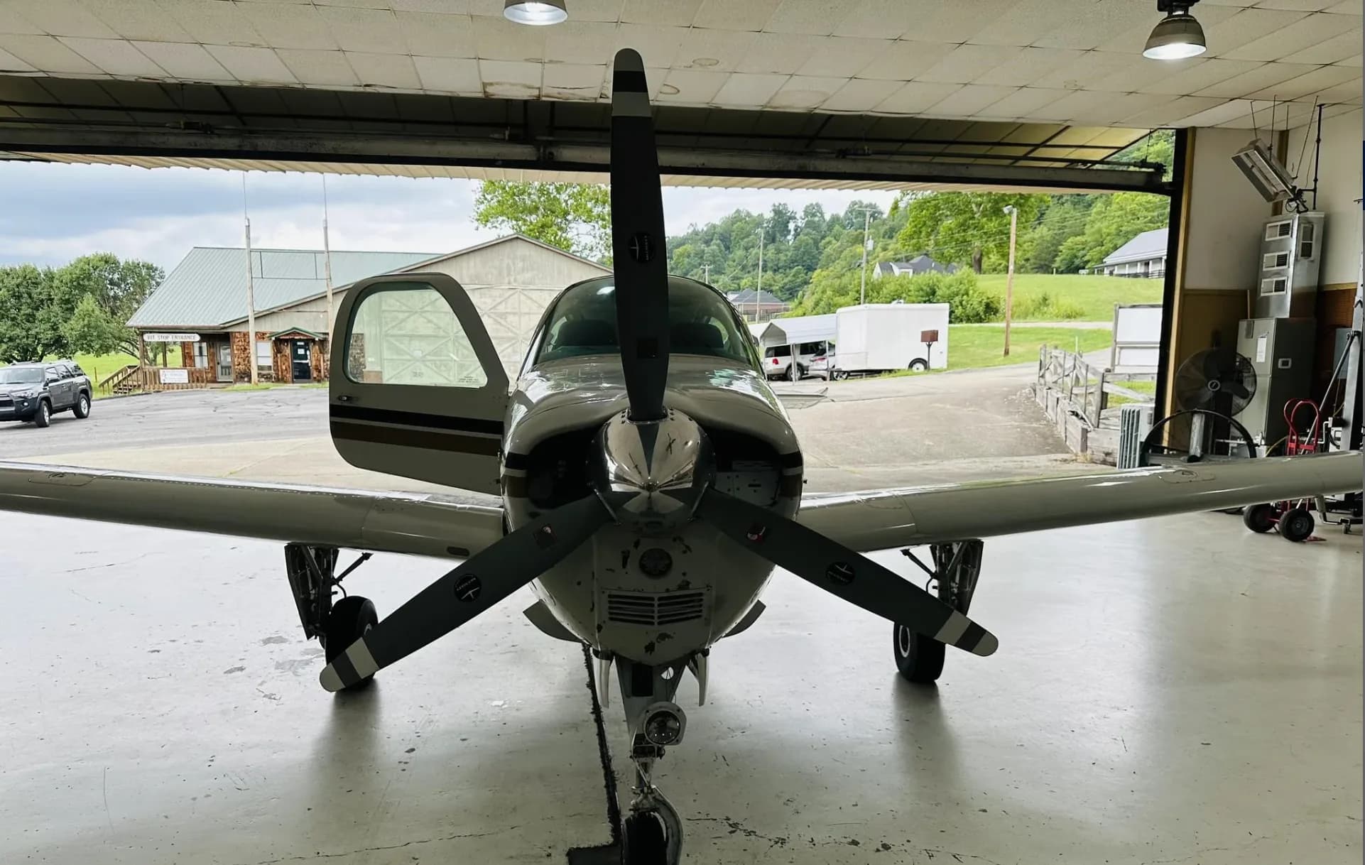 A white and gold Beechcraft Bonanza N7SP with an open door, viewed head-on from inside a hangar.