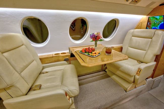 The interior of the aircraft features leather seats, wood trim, and a table with refreshments.