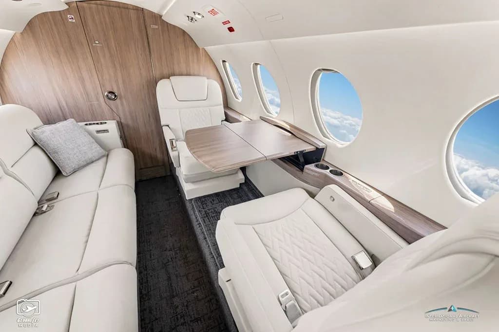 The luxurious white leather interior of a business jet cabin with a side-facing couch and individual seats.