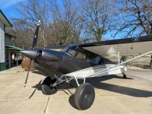 A Carbon Cub aircraft is parked on a concrete pad in front of a building.