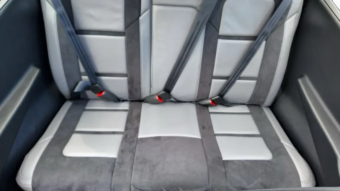 A close-up view of the gray and dark gray rear passenger seats with seatbelts in an aircraft cabin.
