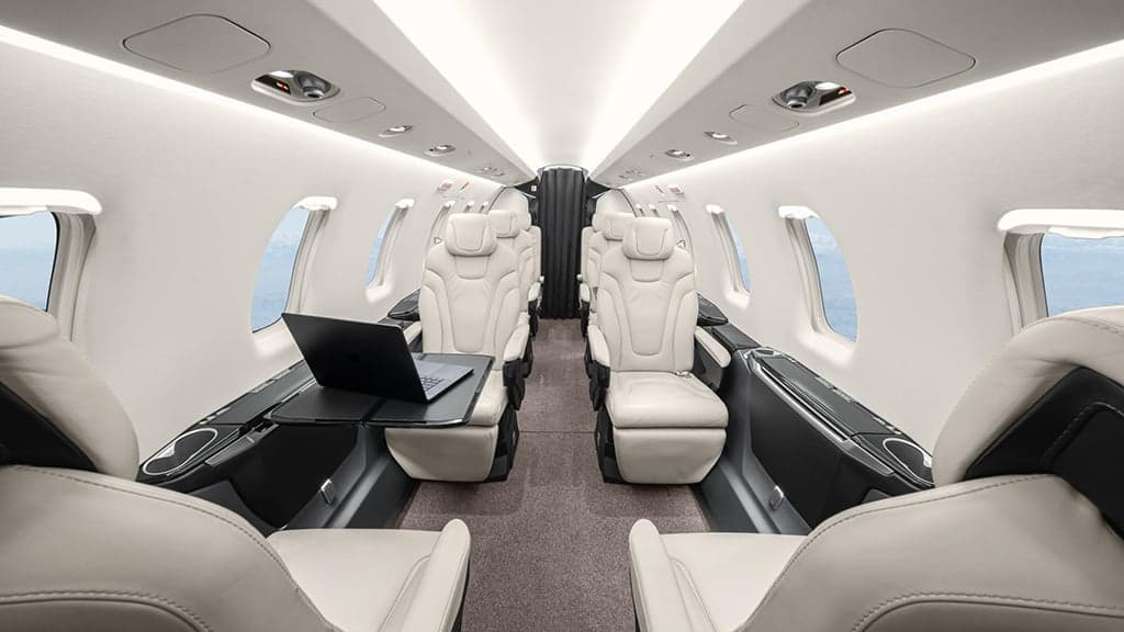 The luxurious interior cabin of a business jet with cream leather seats and a laptop on a table.