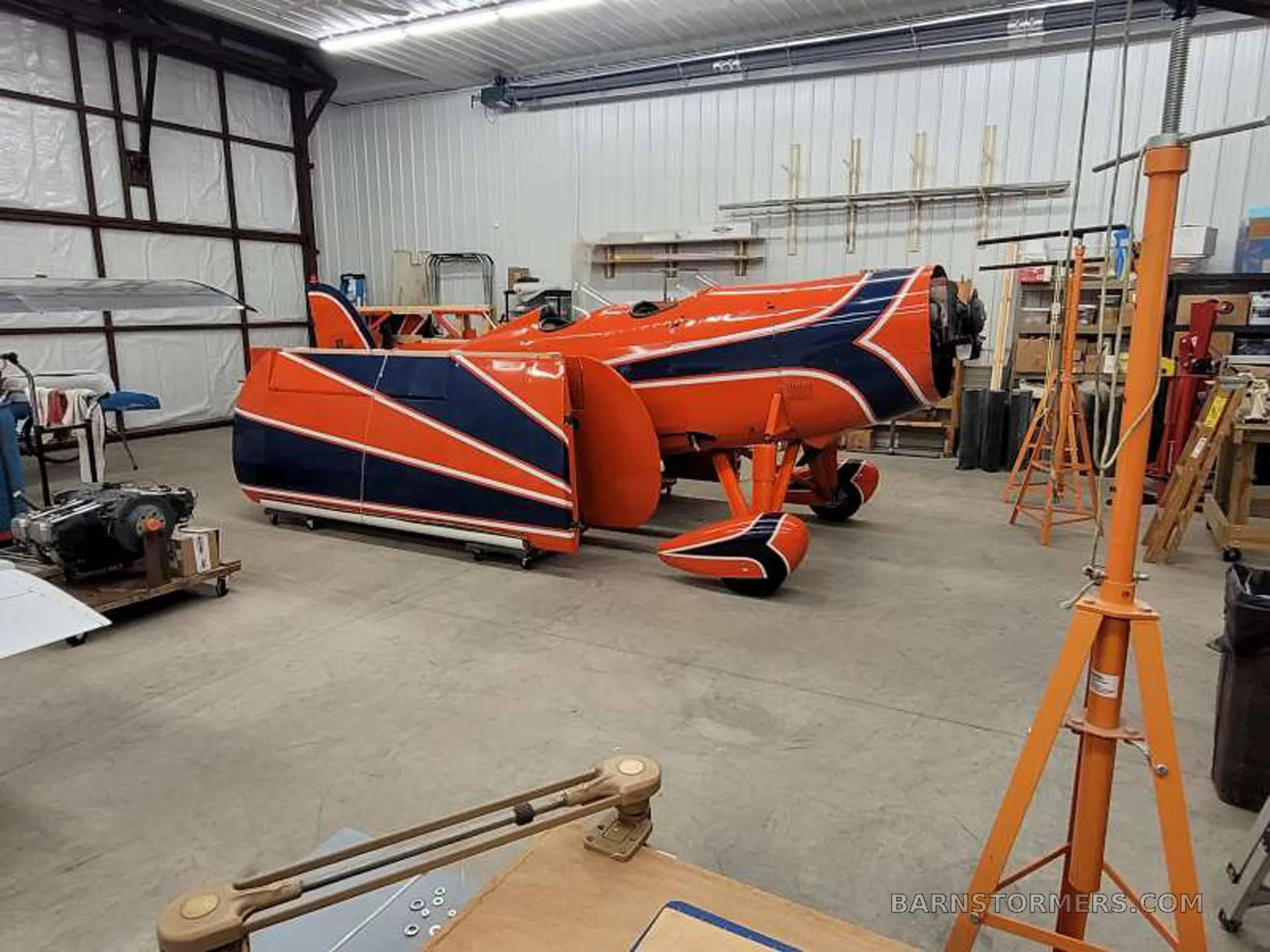 The fuselage and other parts of an orange and blue aircraft are disassembled in a workshop.