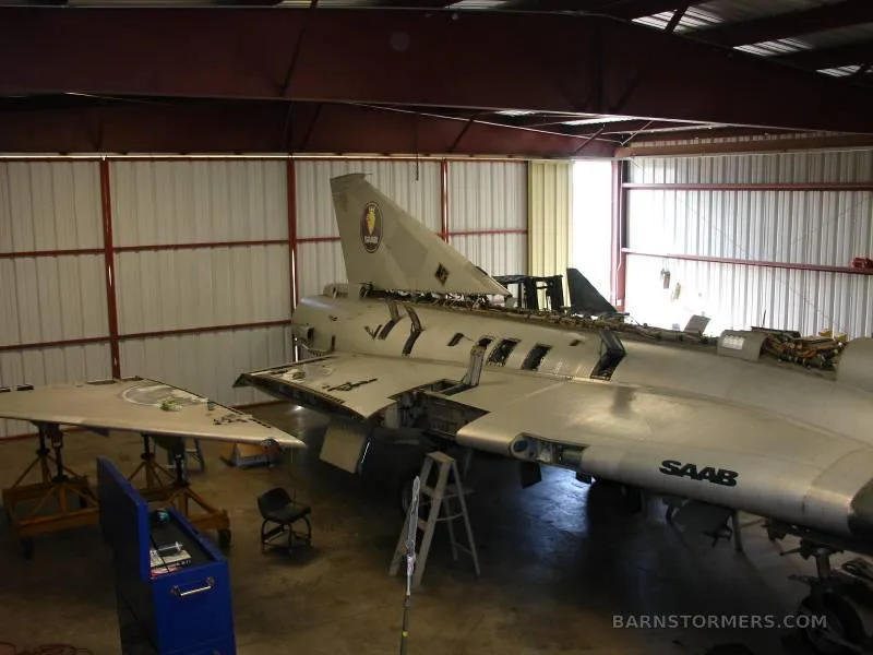 A view of the rear fuselage and tail of a disassembled Saab Draken aircraft in a hangar, with 'SAAB' visible on the side.