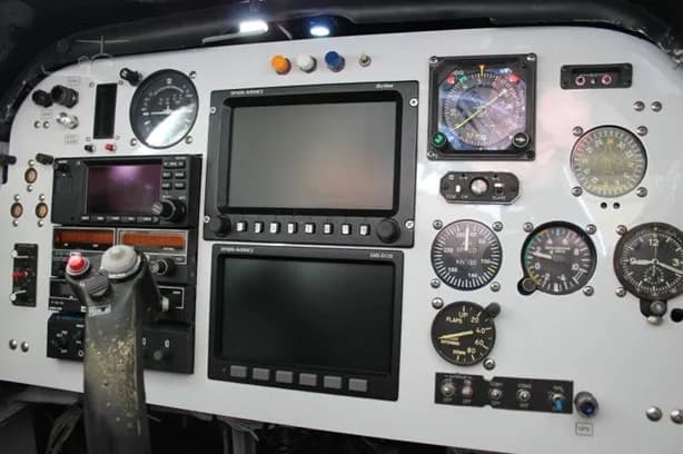A detailed view of an aircraft cockpit instrument panel featuring analog gauges, two large digital displays, and radio equipment.