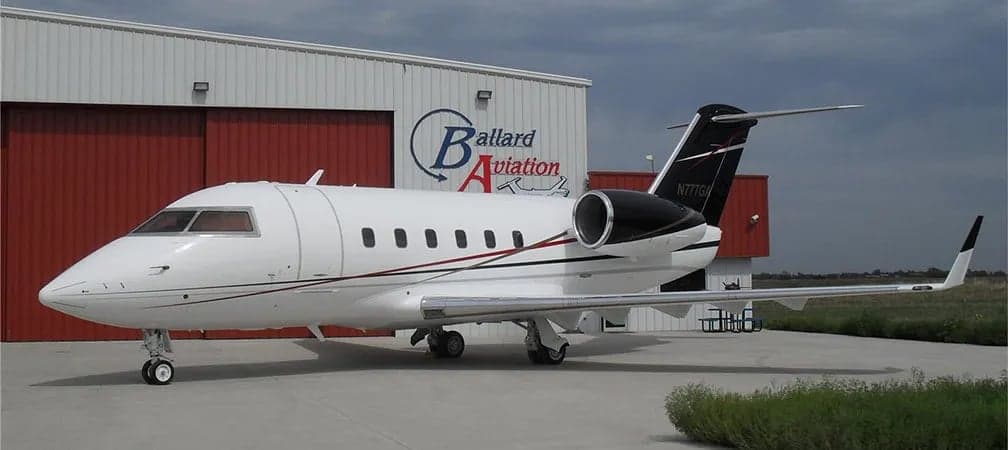 A Challenger aircraft is parked in front of a hangar with the Ballard Aviation logo.