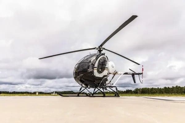 A black and white MD 500 helicopter is parked on the tarmac.