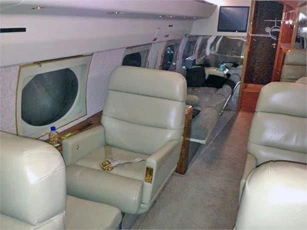 The luxurious interior cabin of a private jet, with light leather seats, a sofa, and wood accents.