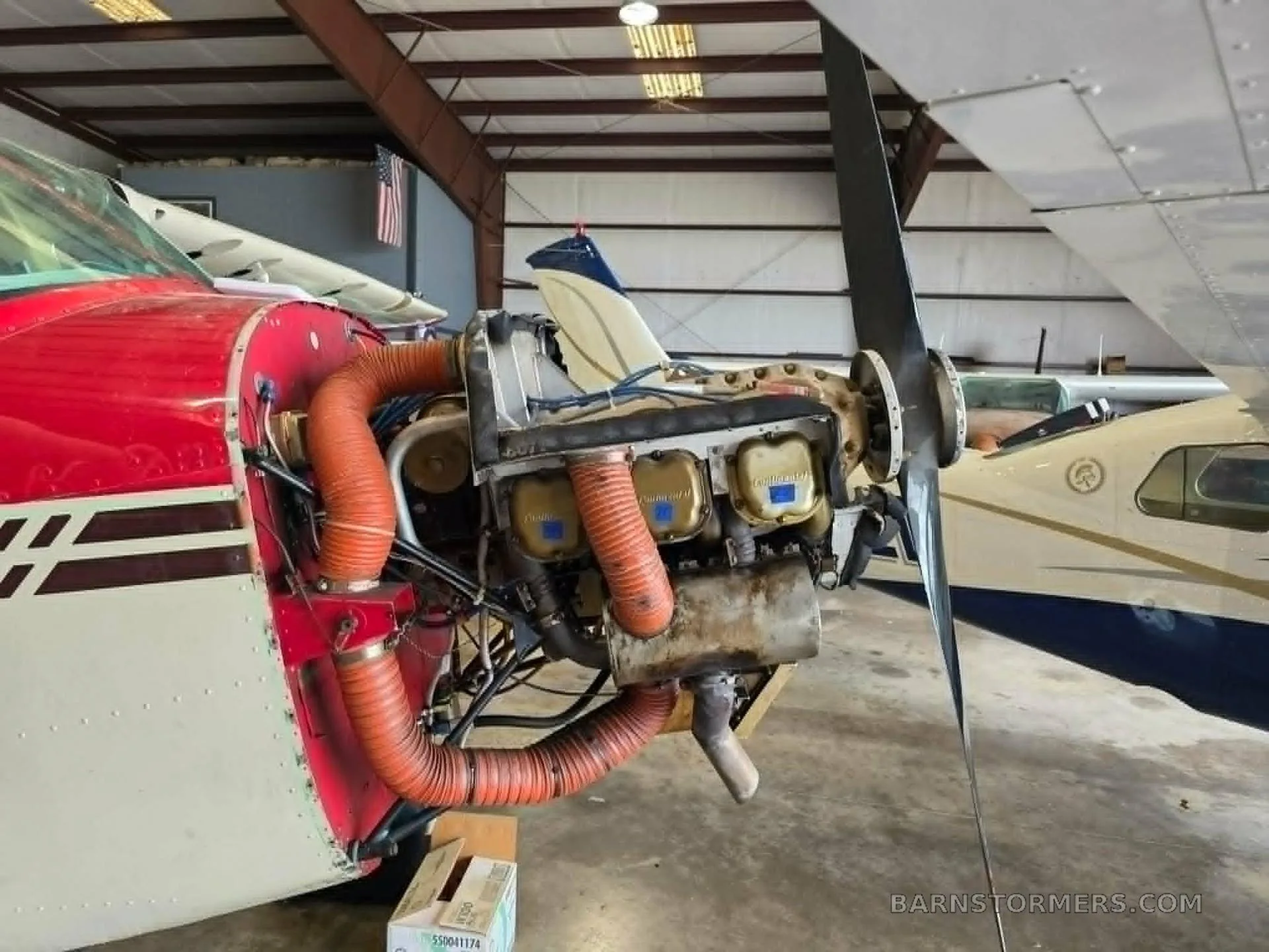 The exposed engine of a red and white propeller aircraft, showing the cylinders and exhaust pipes, inside a hangar.