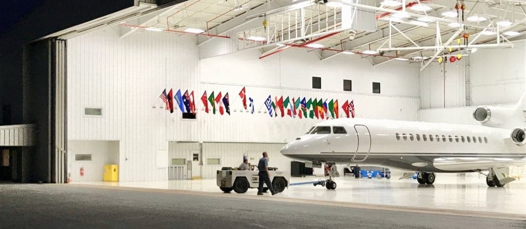 HB-JWX aircraft being towed inside a hangar with international flags.