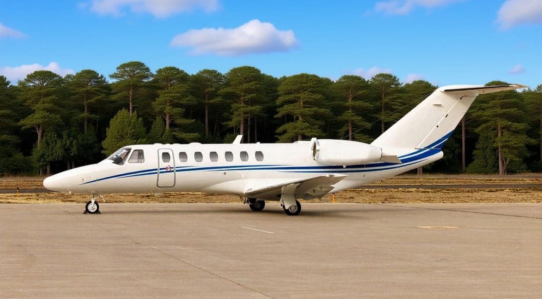 A white Cessna Citation CJ3 sits on the tarmac with a blue stripe.