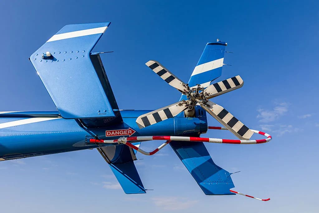A close-up view of the blue helicopter's tail rotor and vertical stabilizer against a clear blue sky.
