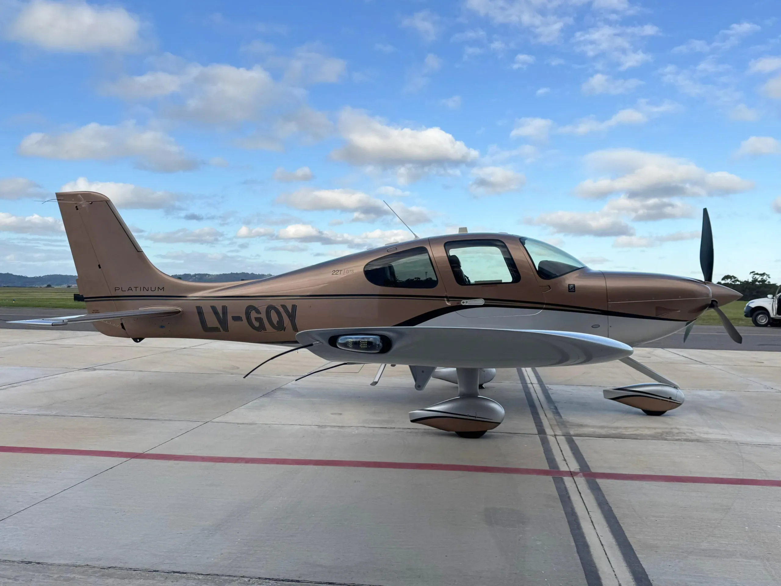 A side view of a brown and silver Cirrus SR22T aircraft with registration LV-GQY on an airport tarmac.