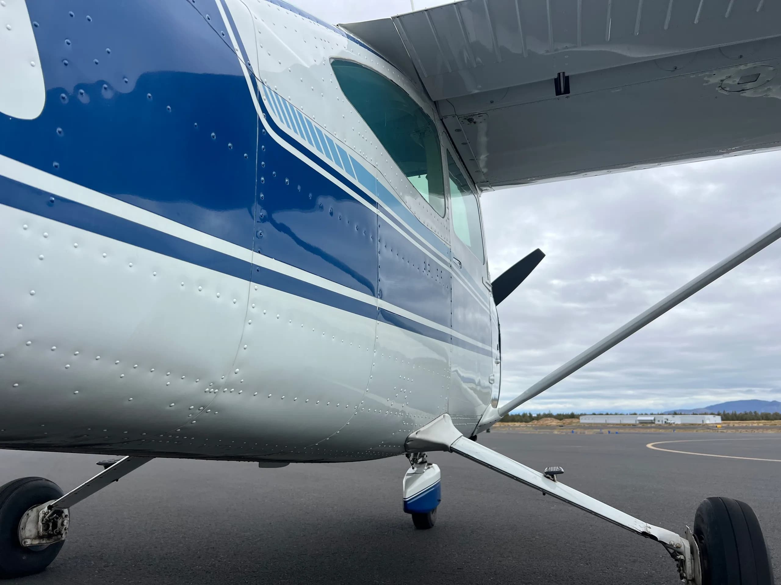 A side view of the fuselage, landing gear, and wing of the blue and white Cessna 172 aircraft.
