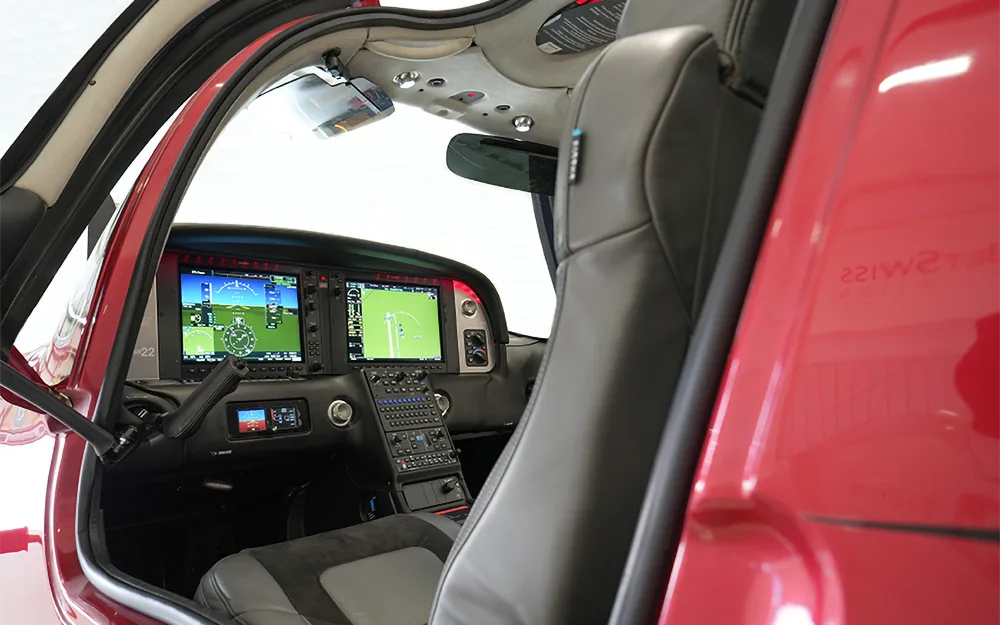 A view into the cockpit of a red Cirrus SR22 aircraft through an open door, showing the instrument panel and front seat.