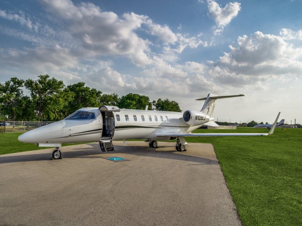 A white business jet (N109EZ) with its main cabin door open is parked on a tarmac under a partly cloudy sky.