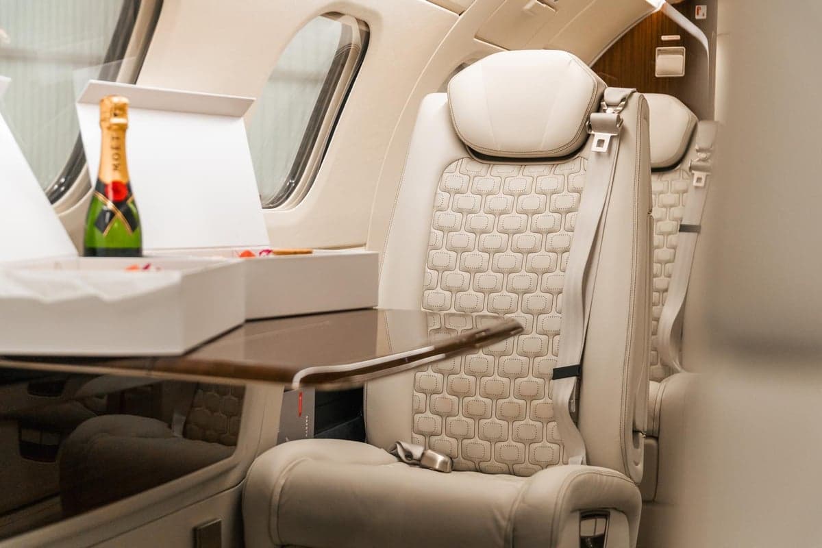 Aircraft cabin interior with cream-colored leather seats and fold-out tables.